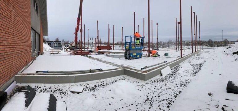Kraftig byggearbeid på en byggeplass i snøvær med konstruksjon av støttemur og rammer for framtidig bygning.